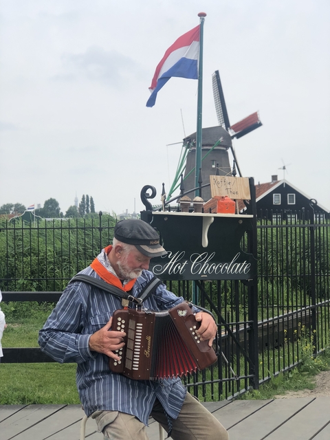 Man with cap standing near a hot chocolate stand with windmills in the background.