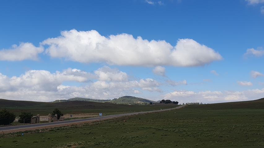       Open landscape with a road leading to distant hills under a clear blue sky.
  