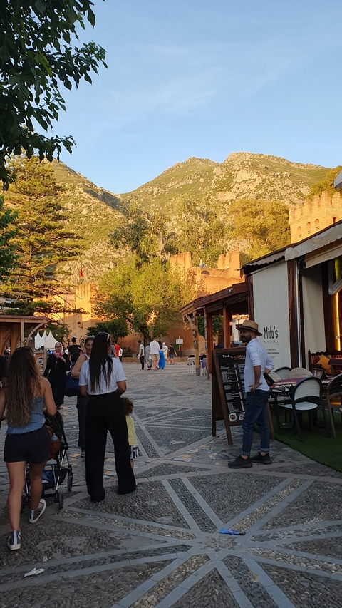       Street scene with people walking and colorful shops.
  