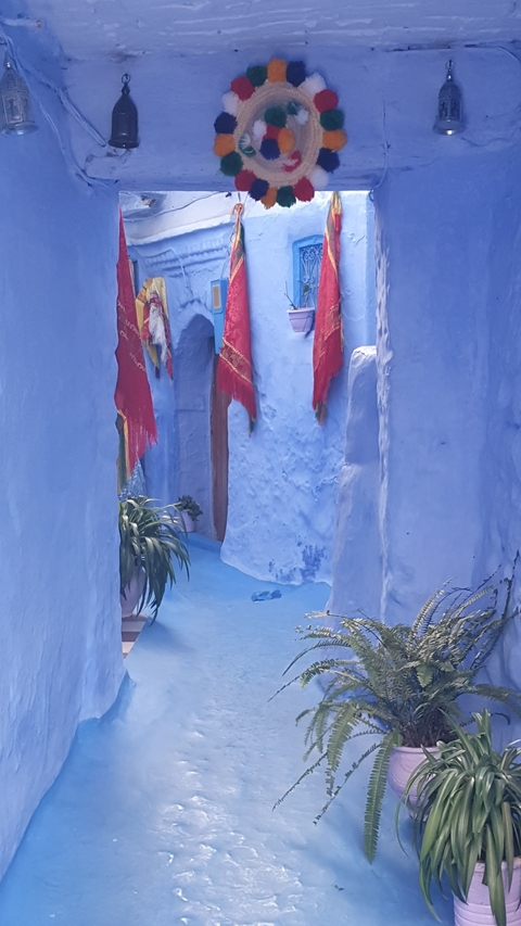       Narrow street with blue painted walls and red flags.
  