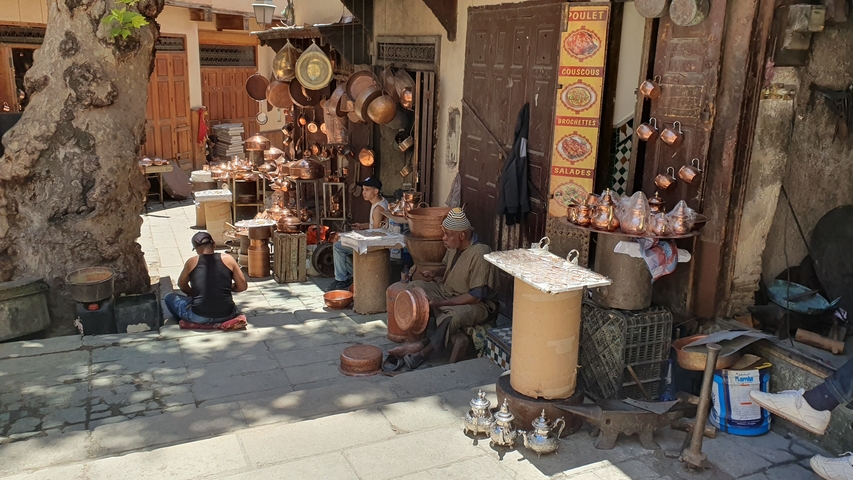 Outdoor market area with copperware items on display.