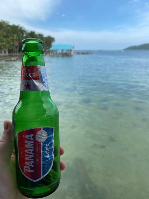       Hand holding a bottle of Panama beer by the ocean.
  