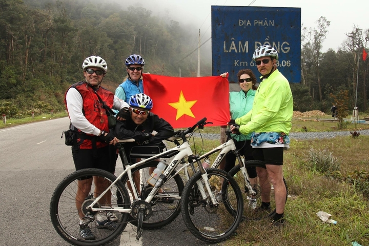 Cyclists posing with a flag in front of a road sign.