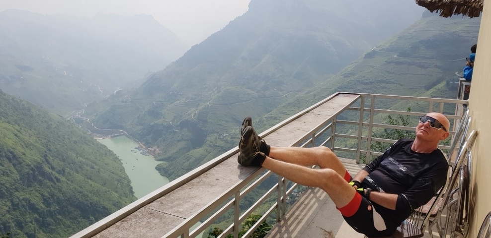 Person relaxing on a railing with a mountain river view.
