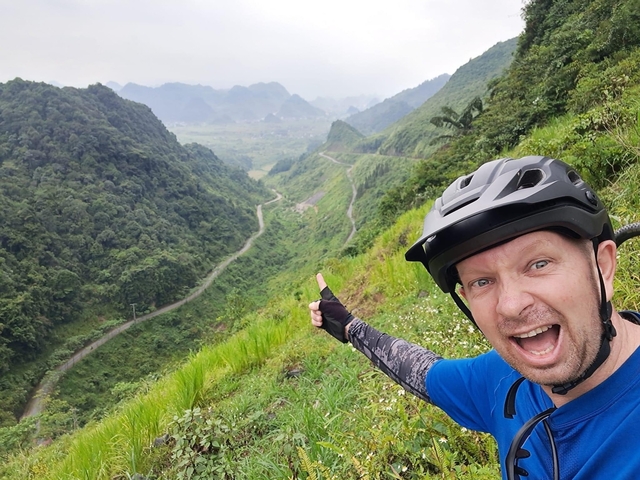       Excited cyclist pointing towards a winding road in the mountains.
  