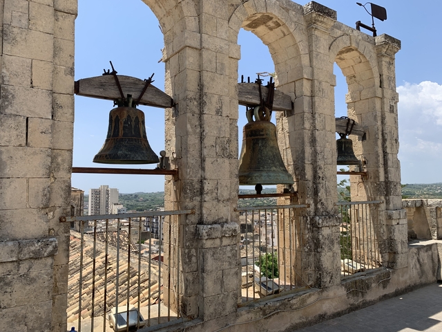       Large church bells with a city view in the background.
  