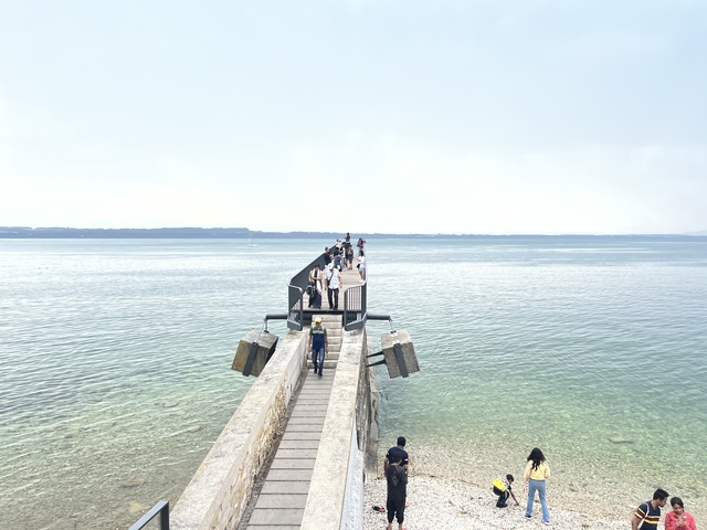       A group of people walking on a pier over a large body of water.
  