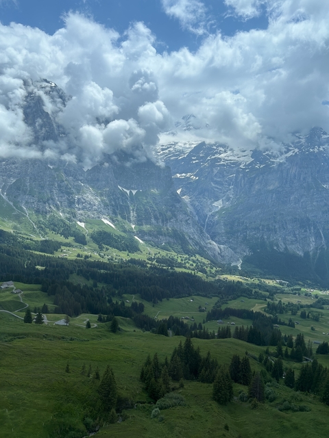       A mountainous landscape with patches of snow atop green valleys.
  