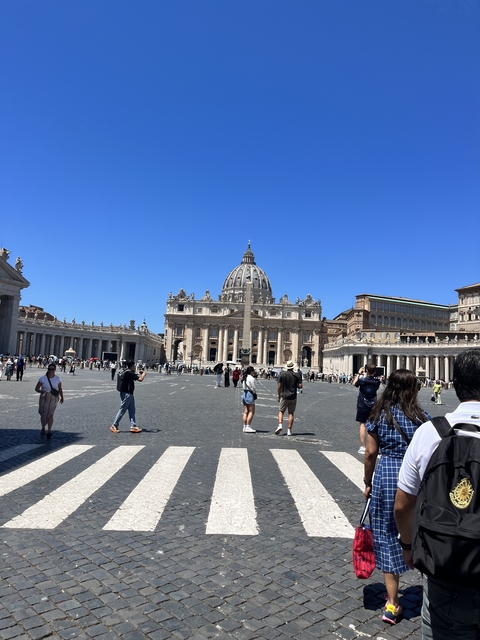       People walking in front of a large dome structure and colonnades.
  