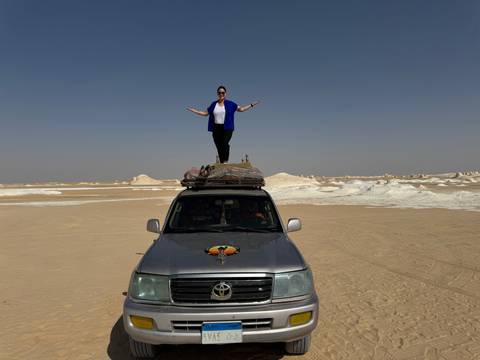       Person posing on top of a car in a desert environment.
  