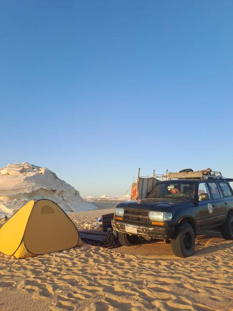 A vehicle and a tent on a desert landscape under a clear blue sky.