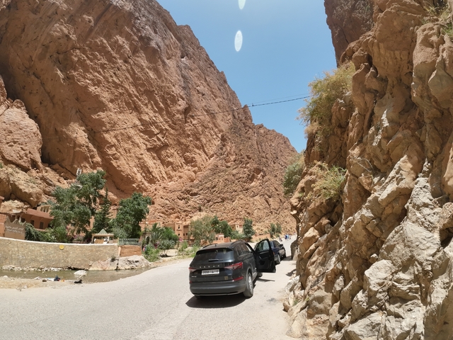       Rocky canyon in a desert climate with cars parked by the road.
  