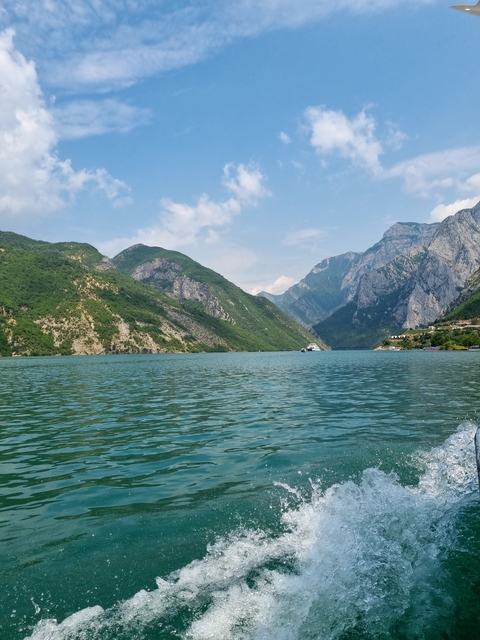       Blue-green waters with a boat and surrounding mountains.
  
