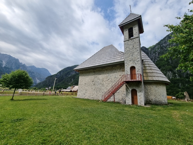       Small stoned church with red stairs in a valley.
  