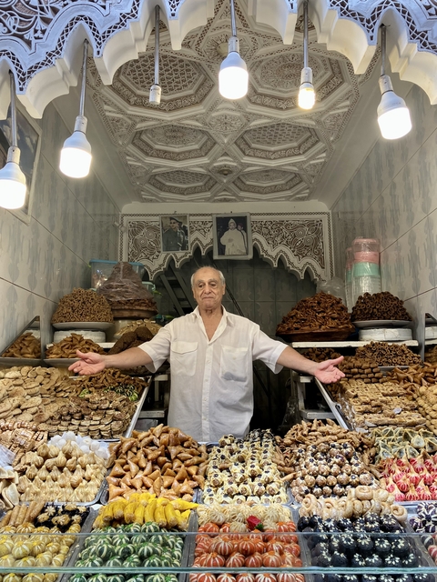 Man in a bakery shop with displayed pastries, in a richly decorated interior.