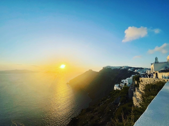       Dramatic sunset over the Aegean Sea with architectural structures on a cliff.
  