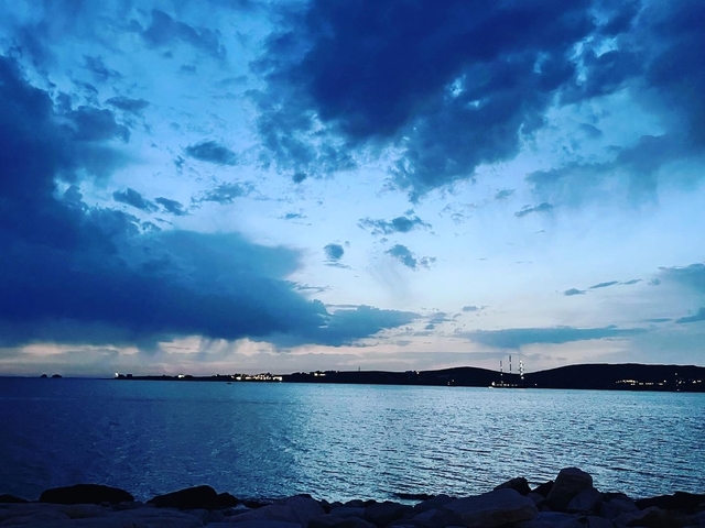       Sunset view over a tranquil sea with a distant land on the horizon.
  
