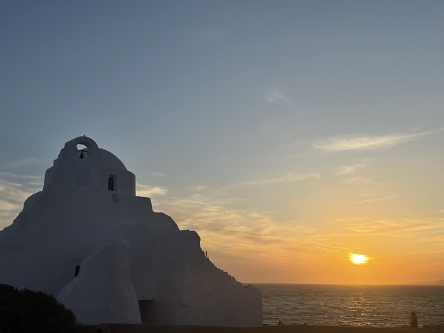       Silhouette of a building against a colorful sunset sky by the sea.
  