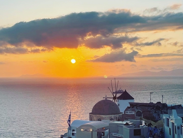       Sunset view over the sea with a domed building and windmill.
  