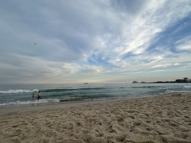       Beach scene with waves and people wading in the water.
  