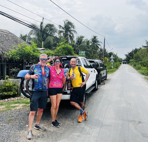 Three people posing with beverages in front of parked cars and palm trees.