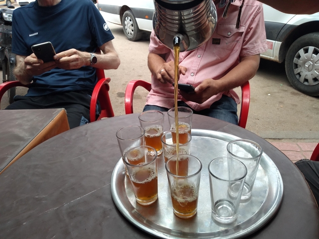People seated around a table with glasses of tea being served.