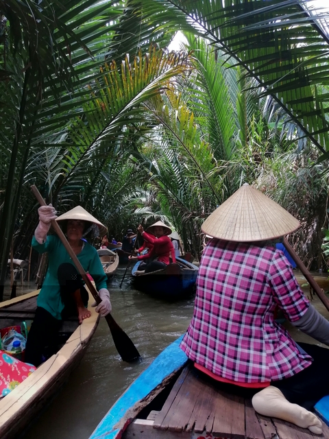       People paddling in small boats through a lush waterway.
  