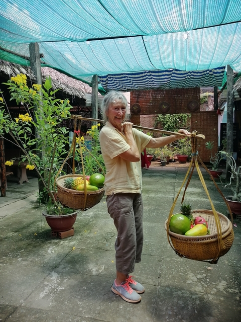       Person carrying a traditional basket with fruit, smiling.
  