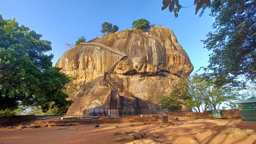 Sigiriya Rock Fortress with a staircase and trees under the clear sky.