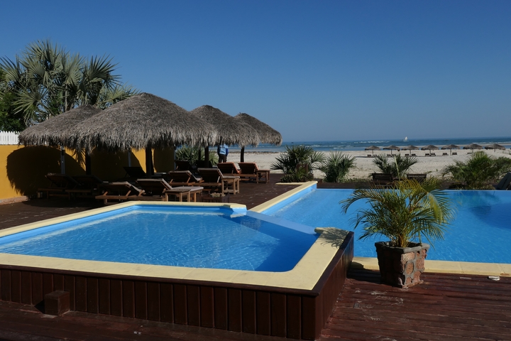       Beachside resort with pool, thatched umbrellas, and loungers.
  