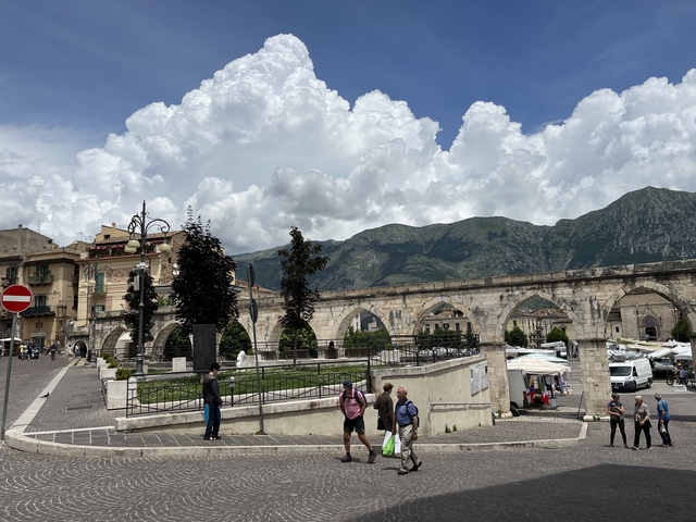 Historical town square with stone arches and mountains.