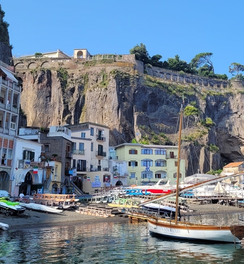       Colorful buildings and boats in a marina with steep cliffs in the background.
  