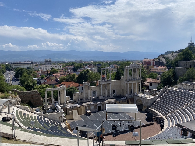 Ancient Roman amphitheater overlooking a city with mountains.