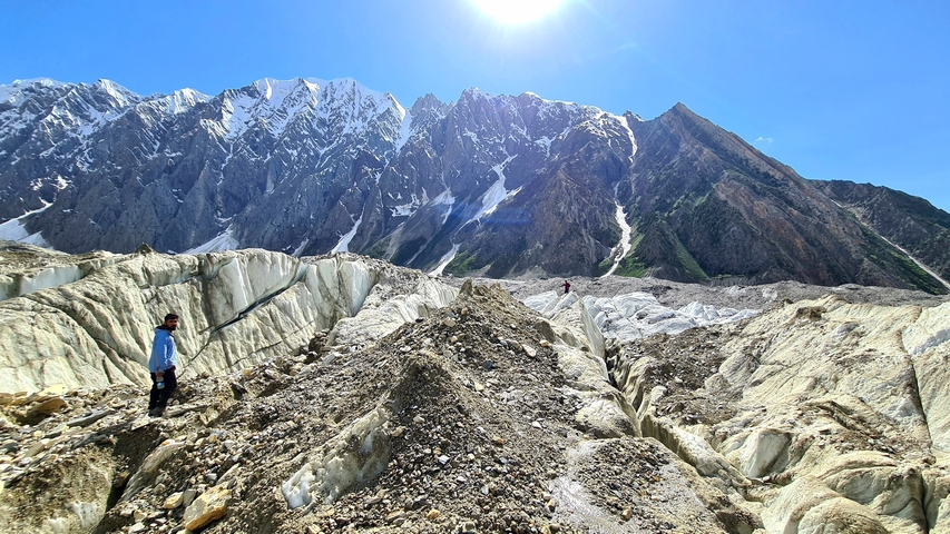       People walking on a glacier with mountains in the background.
  