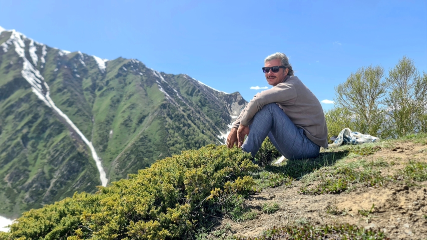       A person sitting on a hill with snow-capped mountains in the background.
  
