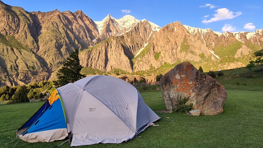 Tents set up on grassy ground with majestic mountains in the background.
