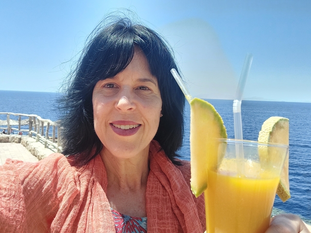       Woman holding a drink with the sea in the background.
  