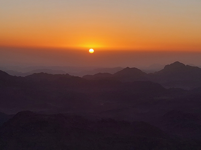 Sunset over mountainous landscape with a glowing sun.