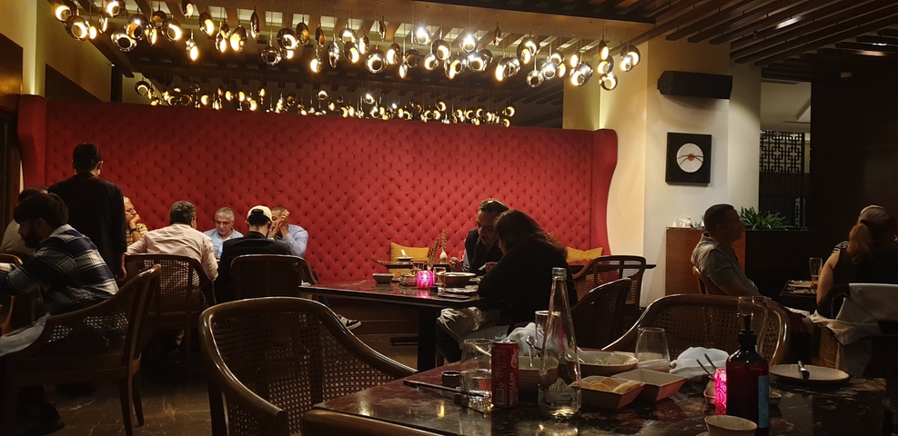       Dimly lit restaurant interior with people dining and unique lighting fixtures.
  