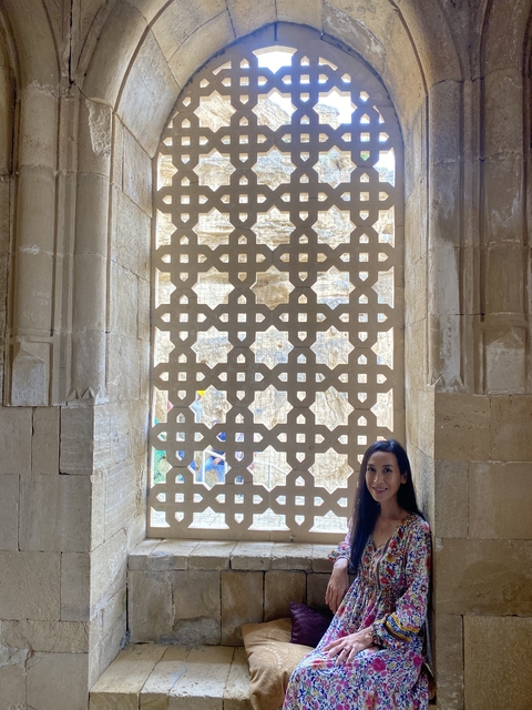       Woman posing near ancient latticework window.
  