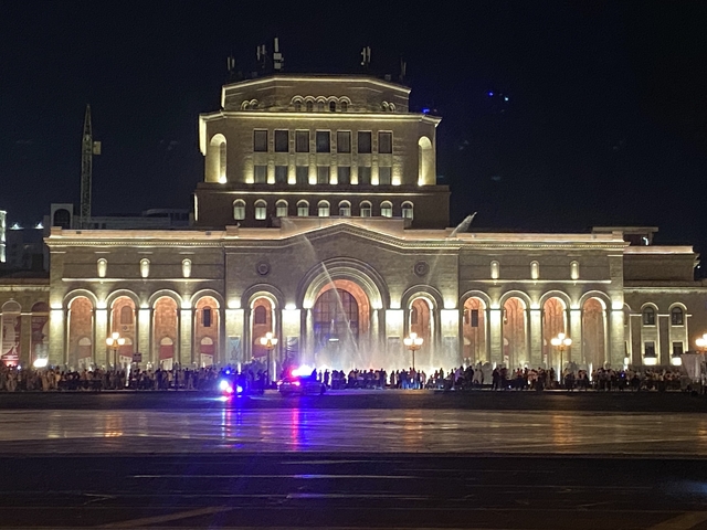       Nighttime view of a grand building with fountains.
  