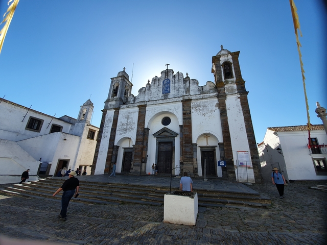 People walking towards a white church with bell towers under a clear sky.