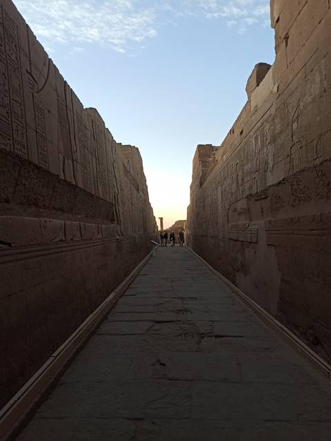 Narrow ancient passage with hieroglyphs leading to a sunset.