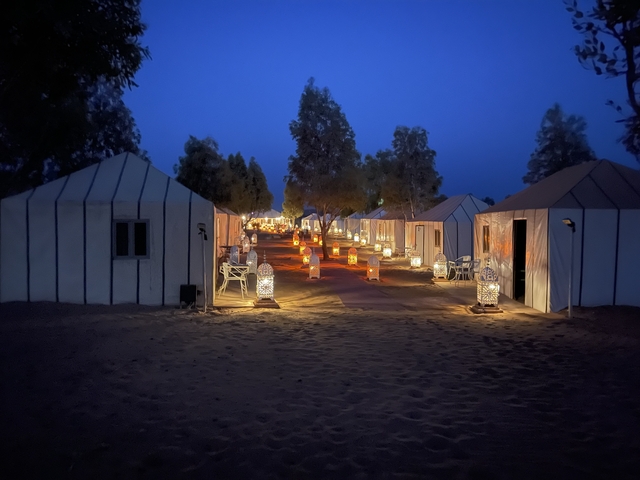 Lantern-lit tents arranged in a desert camp at night.