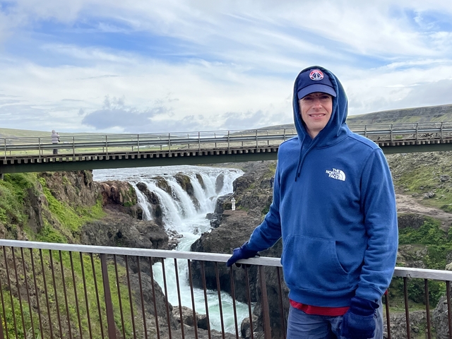       Person posing in front of a waterfall on a bridge.
  