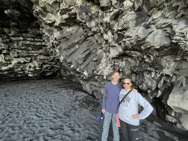       Two people in front of a basalt cave.
  