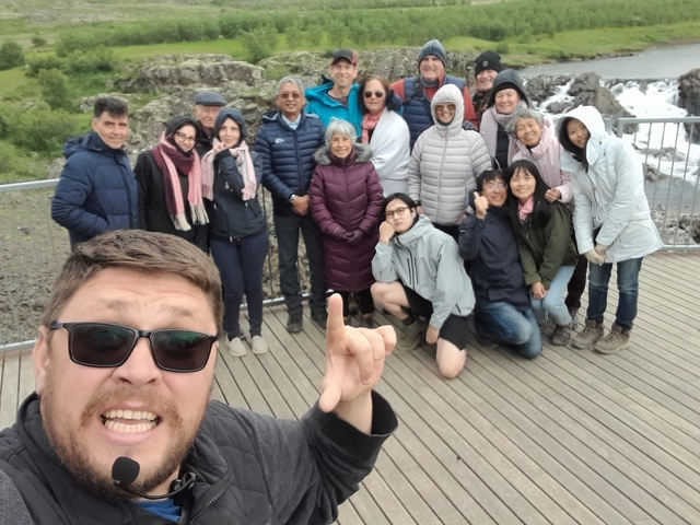       Group of people posing on a wooden platform with a waterfall in the background.
  