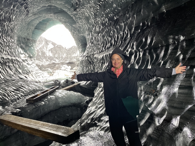       Person standing inside an ice cave with snowy landscape visible outside.
  