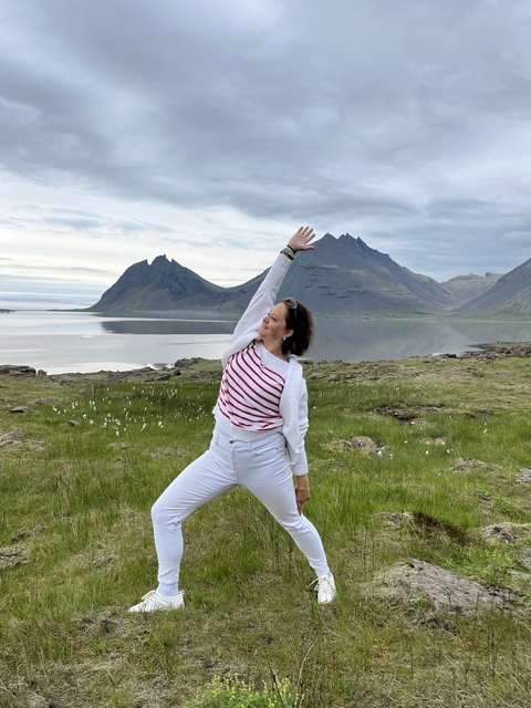       Woman posing energetically in front of mountains and a lake.
  