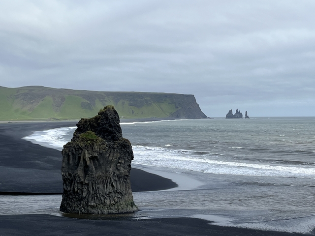       Black sand beach with rock formations and waves.
  